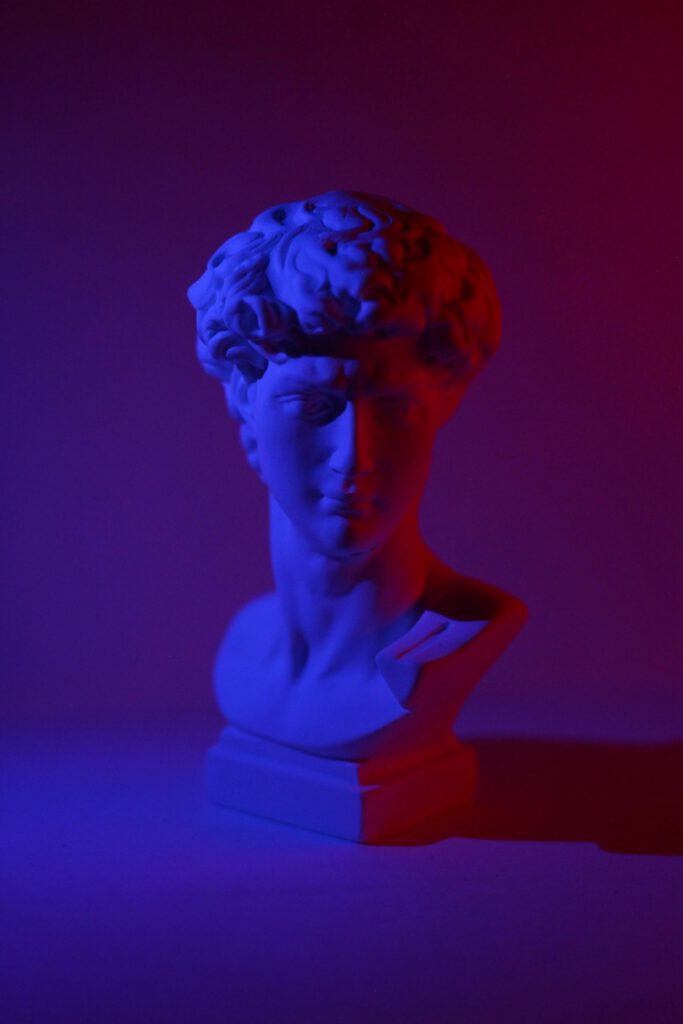 pexels-photo-5665104-5665104 Bust of young male on plinth placed on white surface in dark studio in blue and red lights